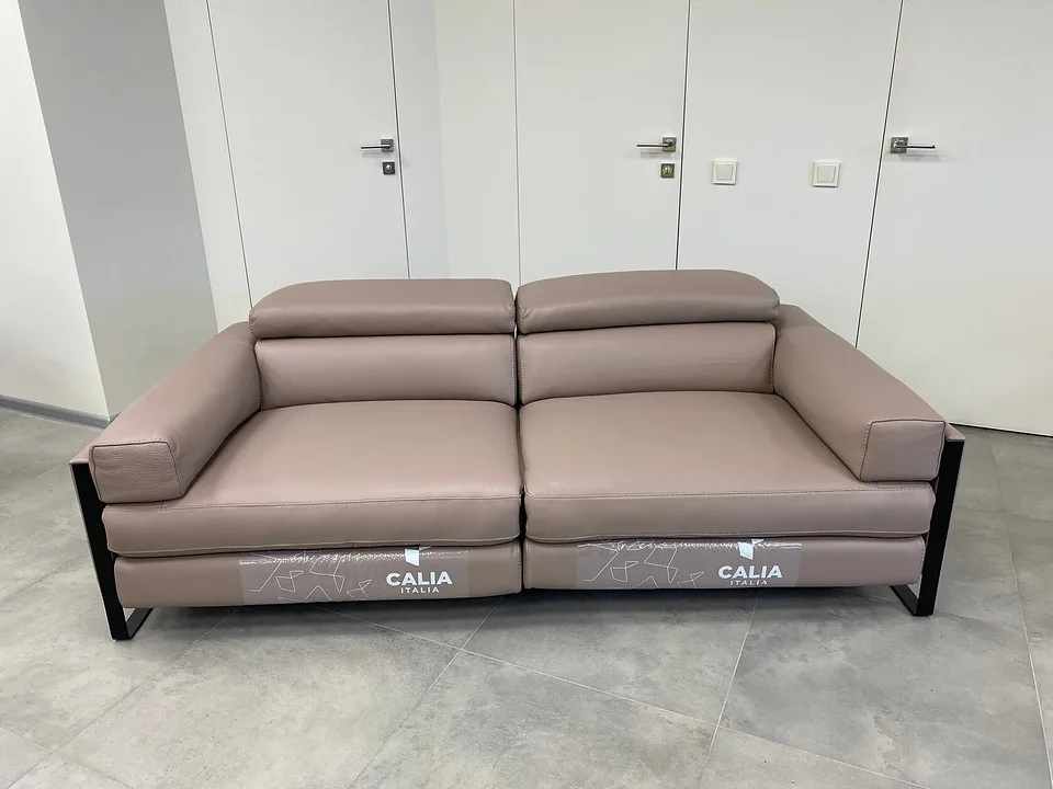 Диван Romeo Relax, Calia Italia, с двумя электрическими реклайнерами, в серо-бежевой натуральной коже в салоне, вид спереди: подголовники опущены, подножья убраны, по бокам чёрные матовые металлические рамы-полозья
