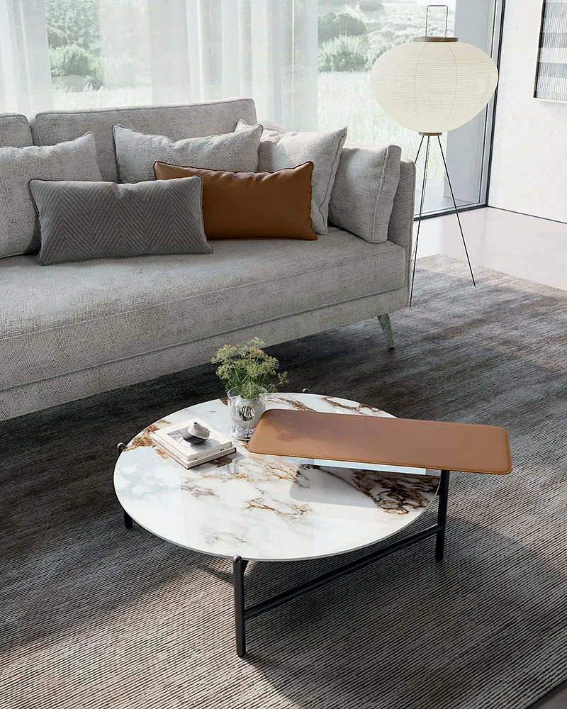 Supernova с круглой светлой столешницей в прожилках, вид спереди сверху: кожаный поднос цвета коньяка выступает за край, тонкие чёрные ножки, позади диван