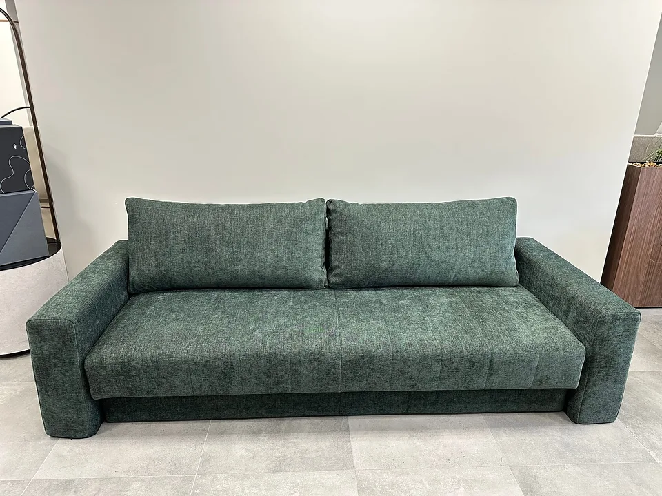 Диван-кровать Akello с подлокотниками в зелёной ткани Avella Pine Green, вид спереди в салоне: две длинные подушки-спинки, широкие мягкие подлокотники