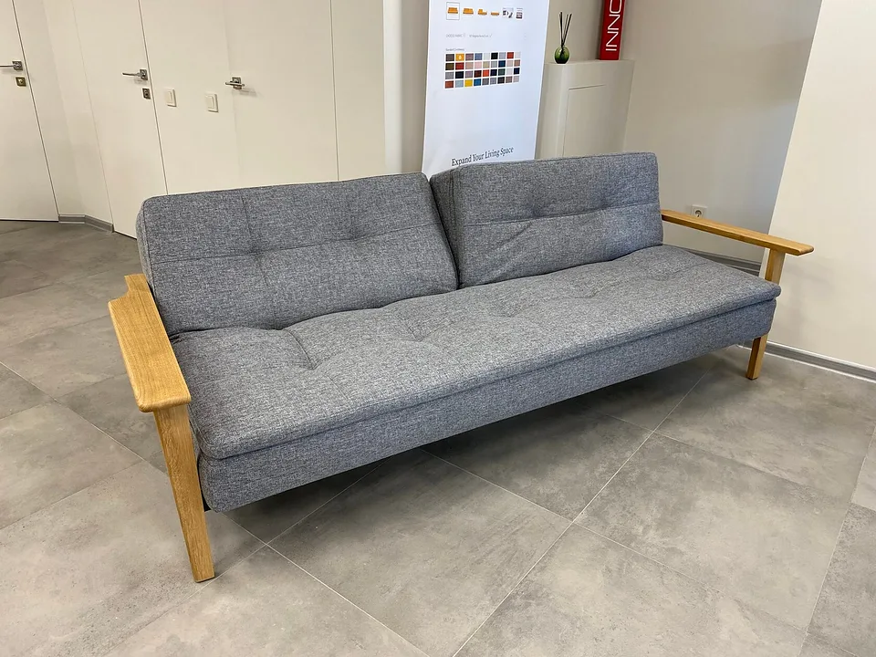 Диван-кровать Dublexo Frej Oak, Innovation Living, в серой меланжевой ткани в салоне, вид спереди-слева: стёганые сиденье и спинка из двух половин, левая откинута сильнее правой, дубовые подлокотники с ножками