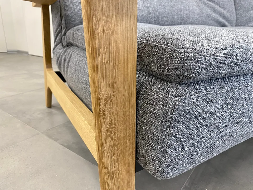 Dublexo Frej Oak крупным планом спереди-слева снизу: дубовая стойка подлокотника, нижняя перекладина боковины и задняя ножка, толстый край сиденья в серой ткани, под ним тёмная стальная рама