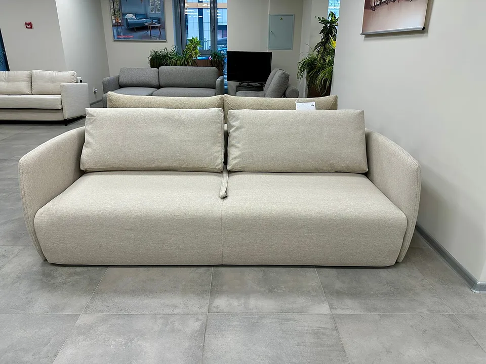 Диван-кровать Salla, Innovation Living, в светлой ткани 584 ARGUS NATURAL в салоне, вид спереди: мягкие округлые подлокотники, две подушки спинки, петля для раскладывания на сиденье