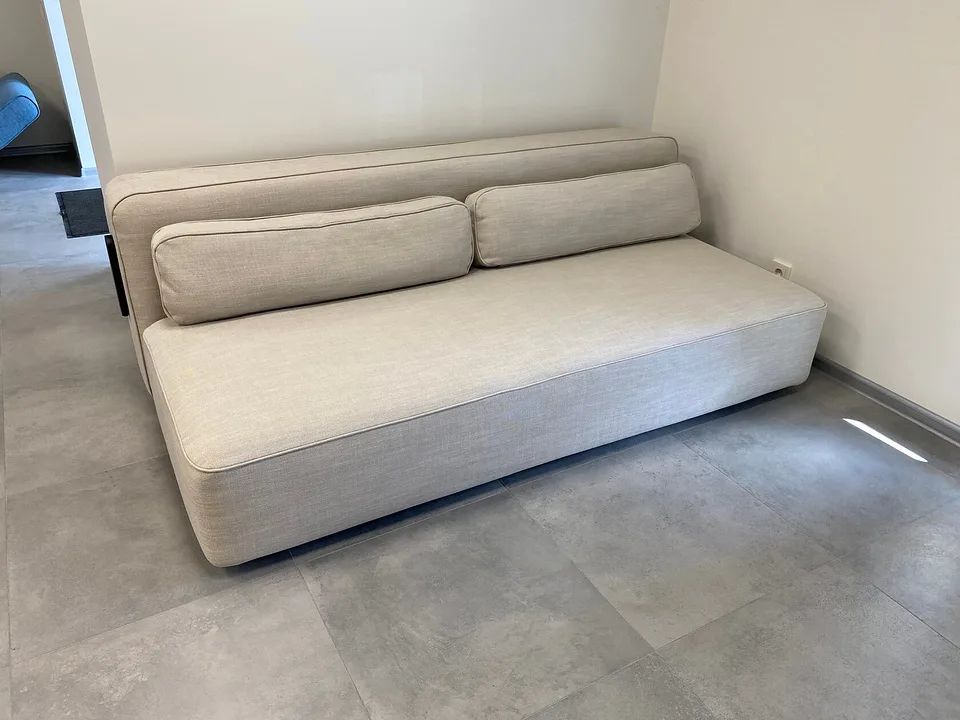 Диван-кровать Yonata, Innovation Living, в светлой ткани Blida Sand Grey в углу салона, вид спереди-слева: глубокое сиденье с кантом, низкая мягкая спинка и две подушки